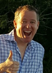 A man giving the thumbs up in front of trees.